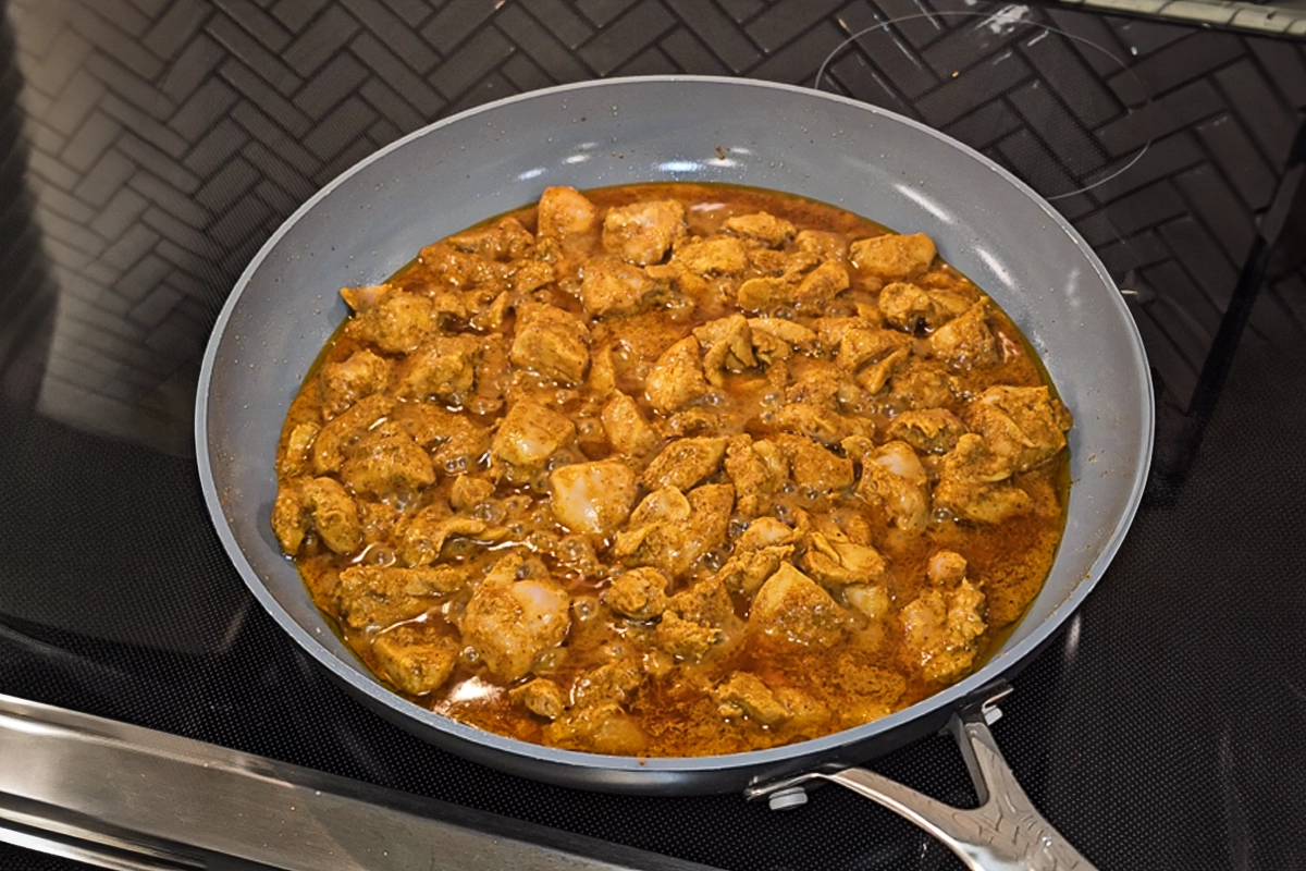 Chicken simmering in a skillet, coated in a rich blend of Indian spices and marinade, as part of Josh Cizek’s butter chicken recipe. The golden curry sauce bubbles gently on a stovetop, signaling the savory depth and aromatic warmth of this homemade classic.