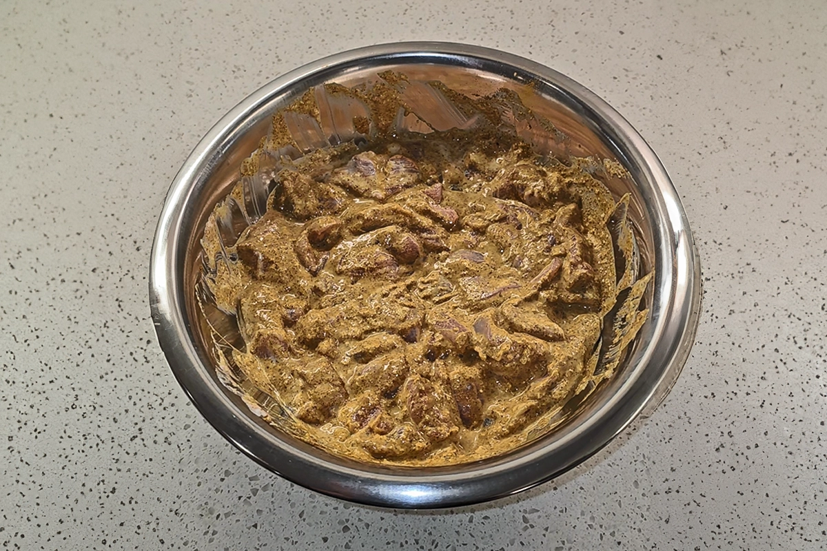 Raw chicken thighs marinating in a creamy spice blend for Josh Cizek’s curry butter chicken recipe, featuring yogurt, lemon juice, Kashmiri chili powder, turmeric, cumin, garam masala, salt, and fresh ginger—captured in a stainless steel bowl on a speckled countertop. This flavorful marinade sets the foundation for a rich, aromatic Indian-inspired dish.