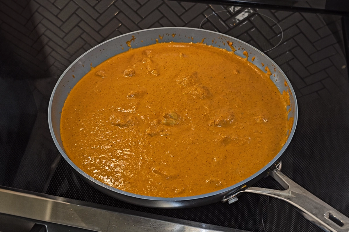 Creamy butter chicken simmering in a skillet, fully cooked and combined with rich, velvety curry sauce as the final step of Josh Cizek’s butter chicken recipe. The golden-orange gravy coats tender chicken pieces, showcasing a homemade Indian dish bursting with flavor, spice, and warmth.