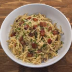 Creamy spaghetti carbonara topped with crispy pancetta, grated Pecorino Romano, parsley, and cracked black pepper in a rustic white bowl.