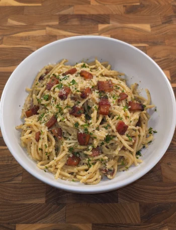 Creamy spaghetti carbonara topped with crispy pancetta, grated Pecorino Romano, parsley, and cracked black pepper in a rustic white bowl.
