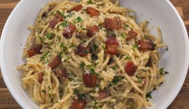 Creamy spaghetti carbonara topped with crispy pancetta, grated Pecorino Romano, parsley, and cracked black pepper in a rustic white bowl.