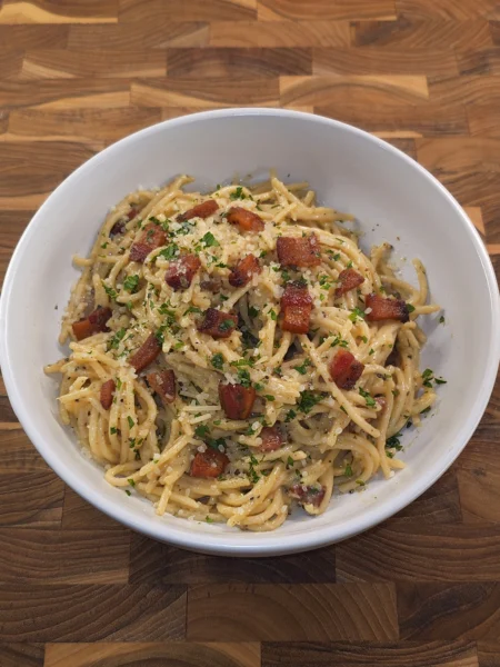 Creamy spaghetti carbonara topped with crispy pancetta, grated Pecorino Romano, parsley, and cracked black pepper in a rustic white bowl.